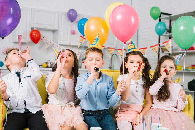 Niños sosteniendo globos de colores y soplando una trompa de fiesta durante el cumpleaños