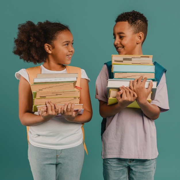 Niños sosteniendo montones de libros.