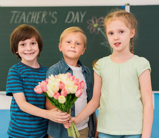 Niños sosteniendo un ramo de flores para su maestra.