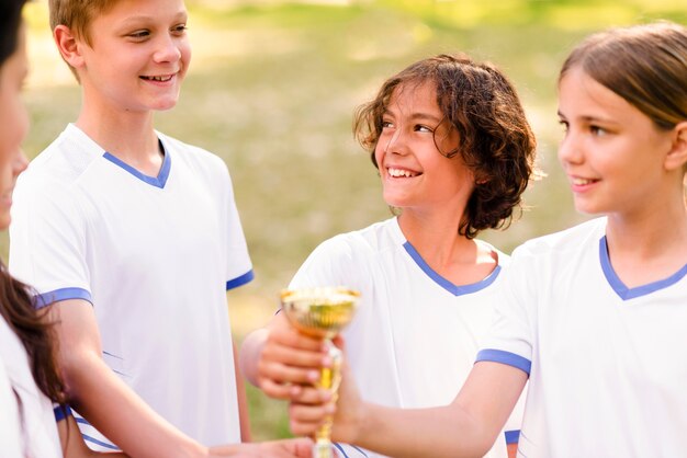 Niños sosteniendo un trofeo de oro.