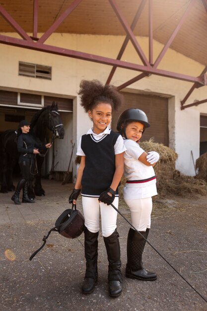 Niños de tiro completo aprendiendo a montar a caballo.