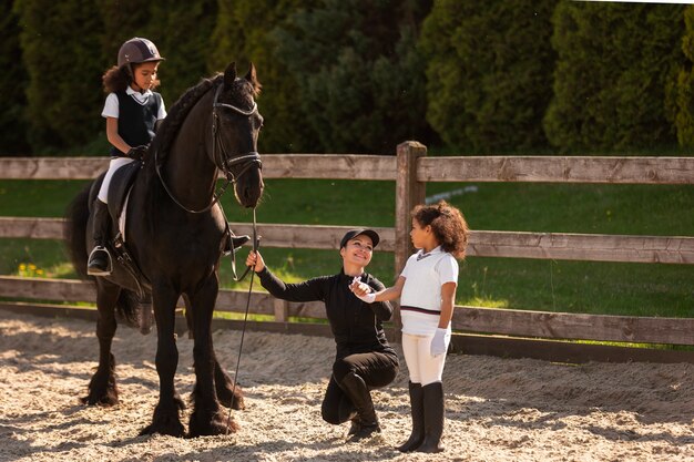 Niños de tiro completo aprendiendo a montar a caballo.