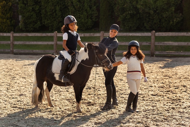 Niños de tiro completo aprendiendo a montar a caballo.