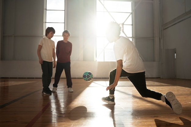 Niños de tiro completo jugando fútbol juntos en el gimnasio