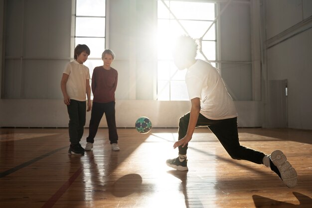 Niños de tiro completo jugando fútbol juntos en el gimnasio