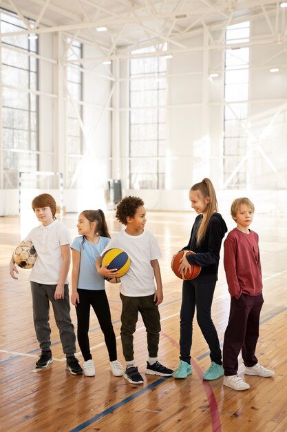 Niños de tiro completo con pelotas en el gimnasio