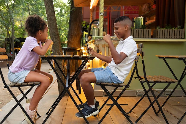 Foto gratuita niños de tiro completo sentados a la mesa con tableta