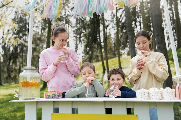 Niños de tiro medio bebiendo limonada al aire libre.