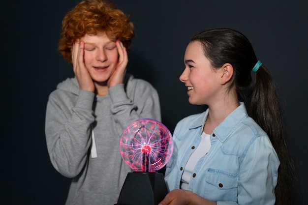 Niños de tiro medio interactuando con una bola de plasma