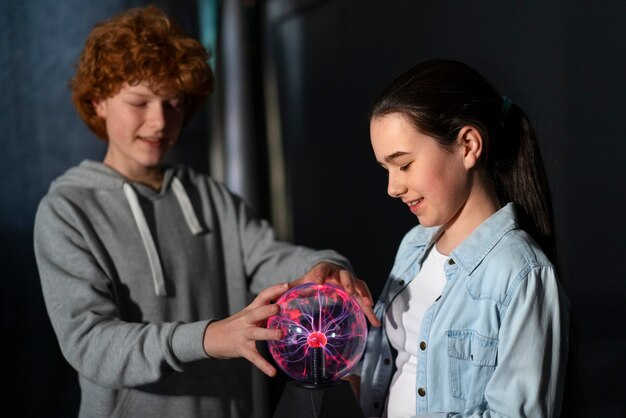 Niños de tiro medio interactuando con una bola de plasma