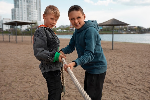 Niños de tiro medio jugando tira y afloja en la playa