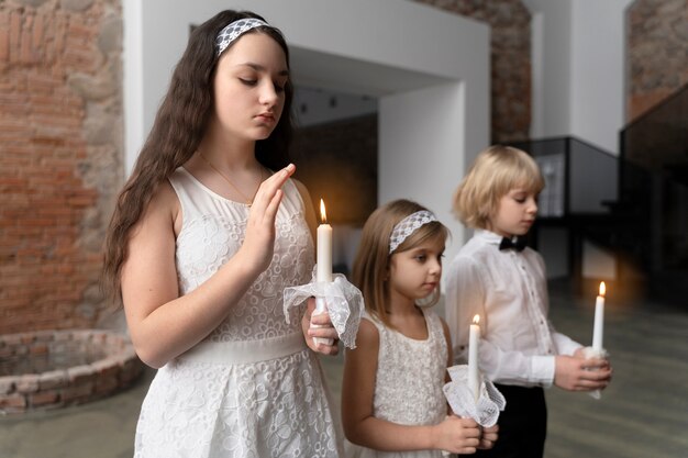 Niños de tiro medio rezando con velas.