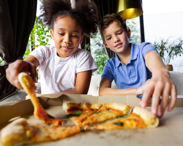 Niños de tiro medio sosteniendo porciones de pizza