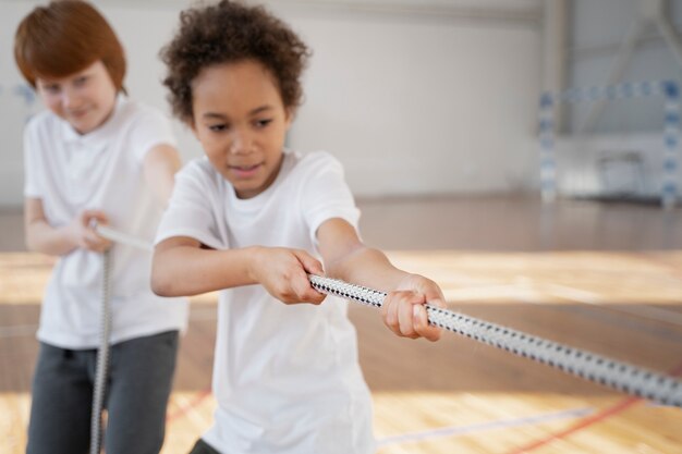 Niños de tiro medio tirando de la cuerda en el gimnasio