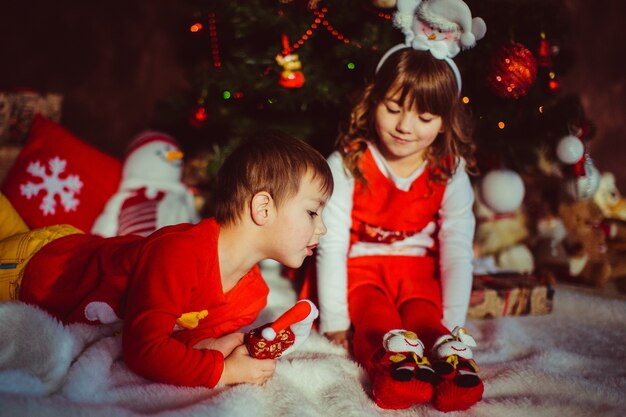 Los niños vestidos de rojo se sientan delante de un árbol de Navidad