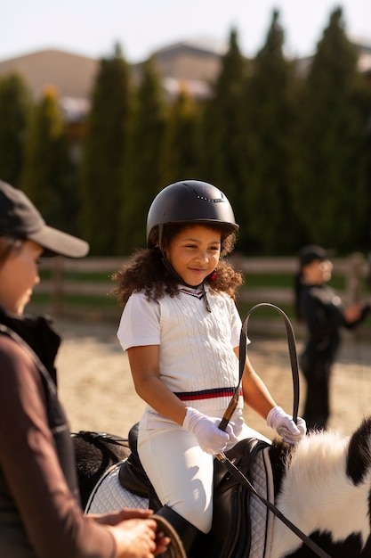 Foto gratuita niños de vista lateral aprendiendo a montar a caballo.