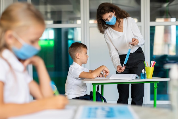 Niños de vista lateral sentados en su escritorio mientras se distancian socialmente