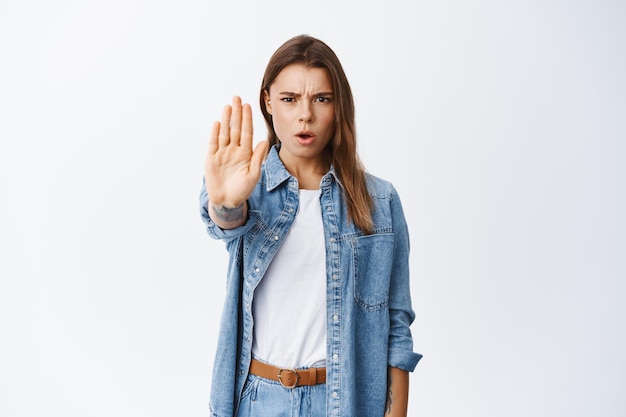 No, detente ahí. Mujer seria haciendo bloque, estirar la mano para prohibir la acción, desaprobar algo malo, de pie en blanco