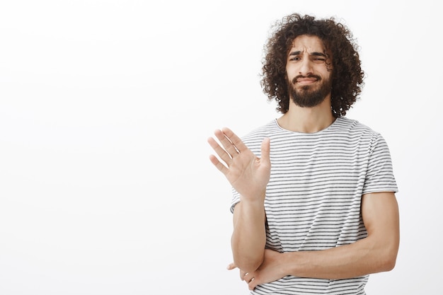 No gracias, paso. Hombre guapo de pelo rizado desinteresado disgustado con elegante camiseta a rayas, agitando la palma en gesto de no o detener, cruzando el pecho con la mano