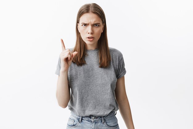 No hagas así más. Retrato de hermosa niña infeliz de pelo oscuro en ropa casual gris gesticulando con la mano, con expresión de la cara enojada.