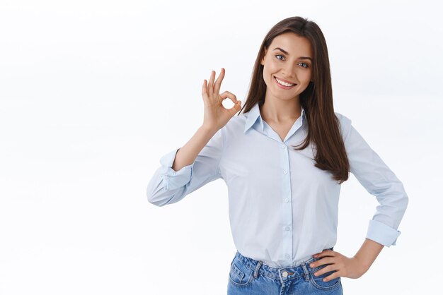 No hay problema. Una joven profesional confiada y relajada asegura que puede lidiar con cualquier cosa por su cuenta. Una dama fuerte y empoderada en el trabajo muestra un gesto correcto y un fondo blanco sonriente y satisfecho.