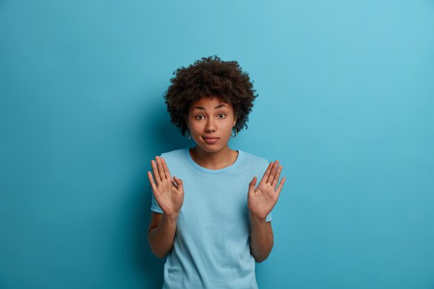 No me involucres en esto. Retrato de mujer de piel oscura despistada levanta las palmas, no quiere meterse en problemas, no se siente culpable después de hacer algo mal, aislado en la pared azul.