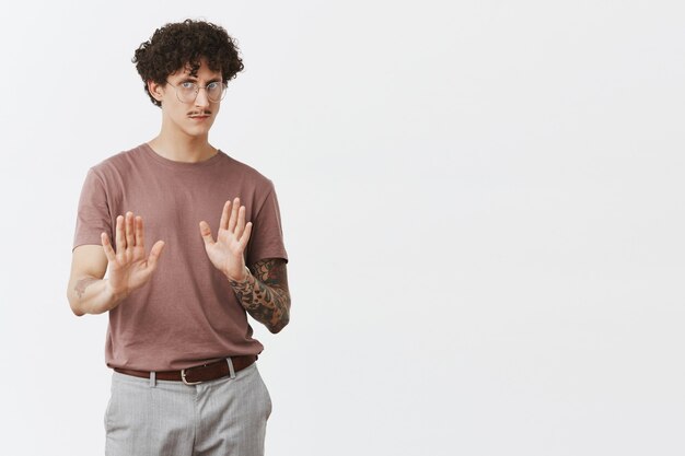 No, me niego. Retrato de guapo disgustado e intenso chico con cabello oscuro y rizado tatuado en el brazo y el bigote tirando de las palmas de las manos para contener y detener el gesto frunciendo el ceño rechazando malos consejos u ofertas