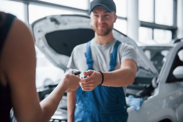 No se preocupe, todo saldrá bien. Mujer en el salón del automóvil con empleado en uniforme azul tomando su auto reparado