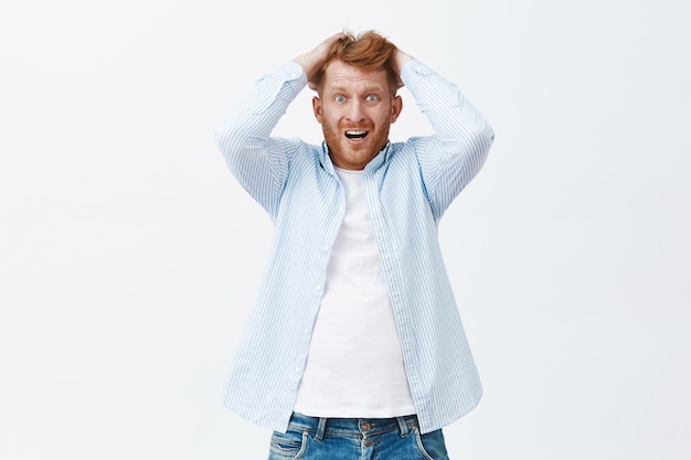 No puedo dejar de entrar en pánico. Retrato de hombre pelirrojo europeo emotivo ansioso con cerdas tirando el cabello de la cabeza, jadeando y frunciendo el ceño sintiéndose angustiado mientras estaba desesperado y tembló sobre la pared gris