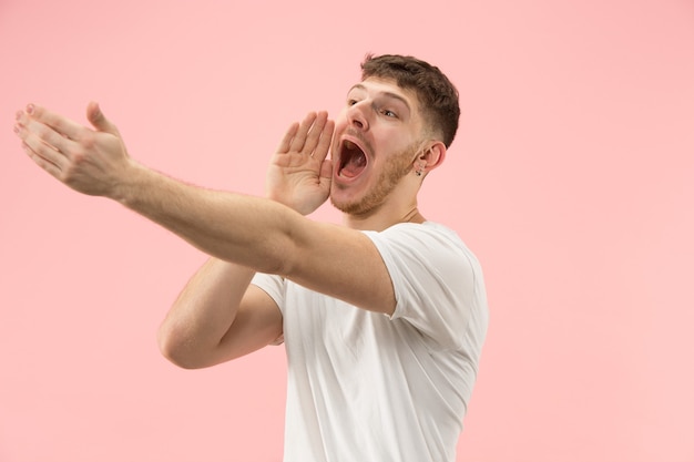 Foto gratuita no te pierdas. joven casual gritando. gritar. hombre emocional llorando gritando sobre fondo rosa de estudio. retrato masculino de medio cuerpo. las emociones humanas, el concepto de expresión facial. colores de moda