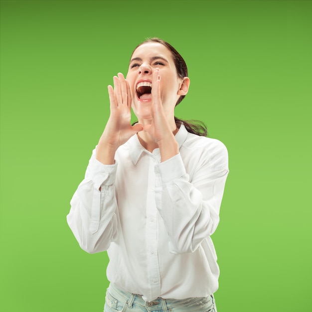 No te pierdas. Joven mujer casual gritando. Gritar. Mujer emocional llorando gritando sobre fondo verde de estudio. Retrato femenino de medio cuerpo. Las emociones humanas, el concepto de expresión facial. Colores de moda