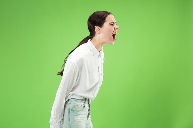 No te pierdas. Joven mujer casual gritando. Gritar. Mujer emocional llorando gritando sobre fondo verde de estudio. Retrato femenino de medio cuerpo. Las emociones humanas, el concepto de expresión facial. Colores de moda