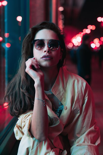 Noche en la ciudad, hermosa mujer entre luces rojas.