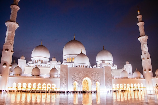 La noche cubre la bella Sheikh Zayed Gran Mezquita iluminada con luces amarillas