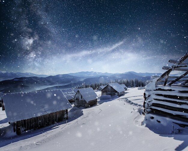 Noche con estrellas. Paisaje de navidad. Casa de madera en el pueblo de montaña. Paisaje nocturno en invierno