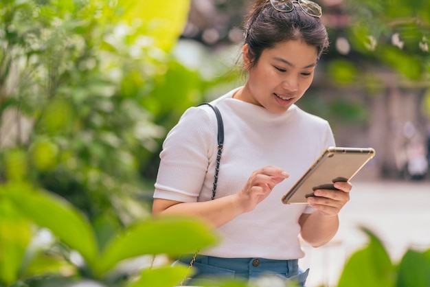 Nómada digital mujer asiática adulta joven que trabaja en cualquier lugar comunicación mano usando tableta contacto en línea y reunión con nuevo estilo de vida alegre felicidad en café parque jardín concentrado enfoque trabajo