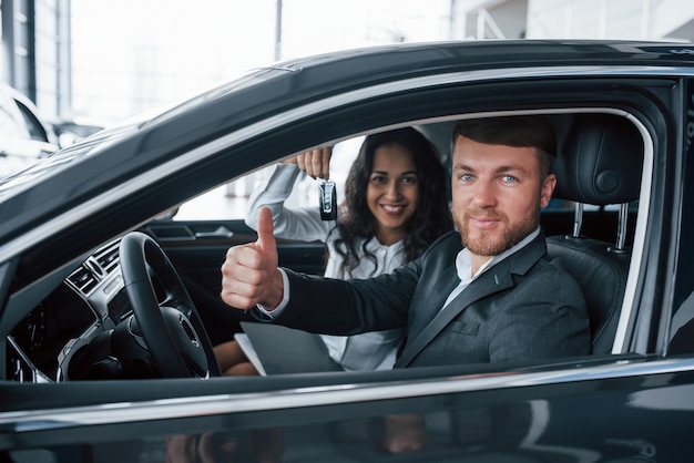 Nos gusta esto. Encantadora pareja exitosa probando coche nuevo en el salón del automóvil