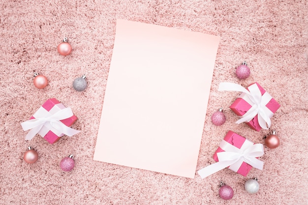 Foto gratuita nota de saludo con cajas de regalo de navidad y bolas sobre una alfombra con textura rosa