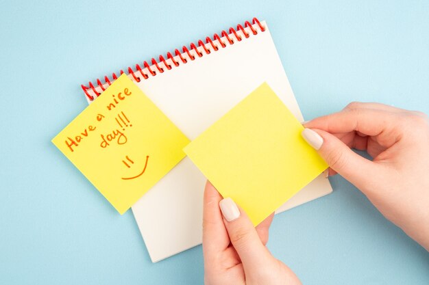 Las notas adhesivas del cuaderno espiral de la vista superior en la mano de la mujer tienen un buen día escrito en papel de nota amarillo en azul