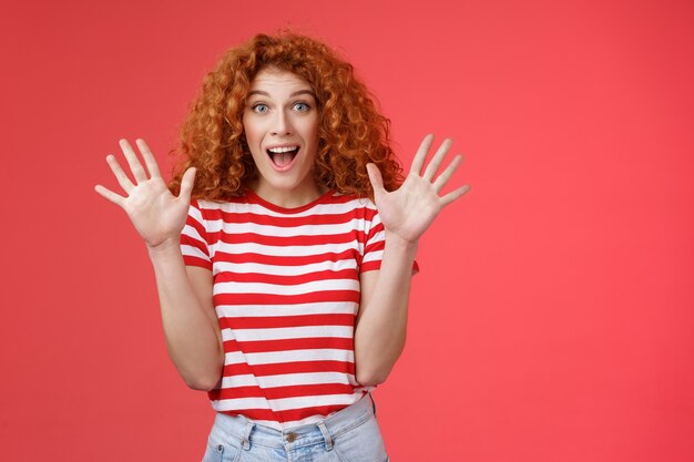 Foto gratuita noticias extremadamente maravillosas que ella emocionó. emocionada emotiva hermosa mujer pelirroja grito asombrado asombrado sorpresa levantar manos agitando impresionado boca abierta mirada fascinada fascinada fondo rojo.