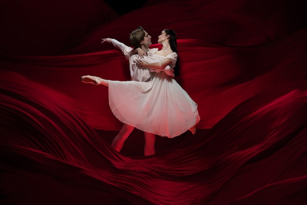 Novela. Bailarines de ballet jóvenes y agraciados en la pared de tela roja en acción clásica. Arte, movimiento, acción, flexibilidad, concepto de inspiración. Pareja caucásica flexible con ondulantes ondas rojas.