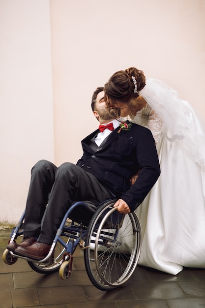 La novia abraza al novio en la silla de ruedas de detrás que presenta en la calle