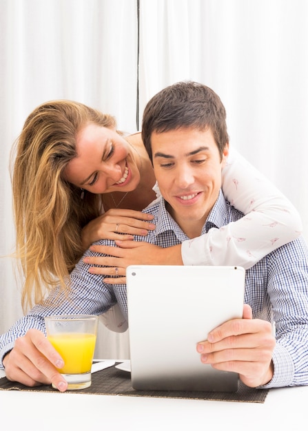 Novia abrazando a su novio sonriente sosteniendo vaso de jugo y tableta digital