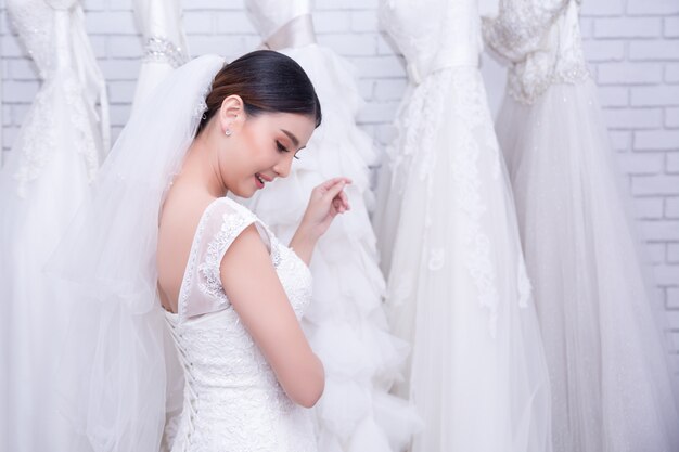Novia asiática de la mujer joven que intenta en el vestido de boda en la boda moderna