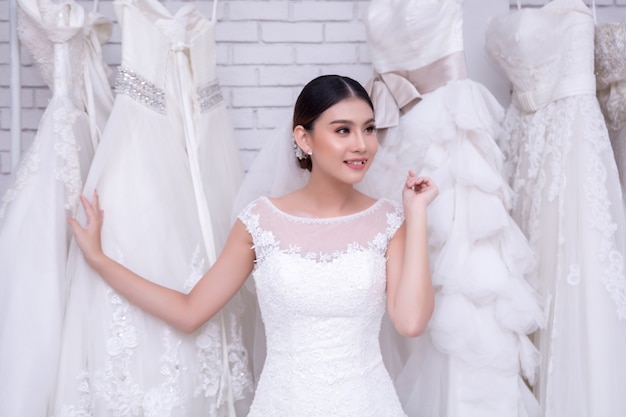Novia asiática de la mujer joven que intenta en el vestido de boda en la boda moderna