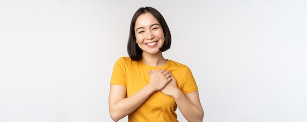 Novia asiática romántica cogidos de la mano en el corazón sonriendo con cuidado y ternura de pie en camiseta amarilla sobre fondo blanco.