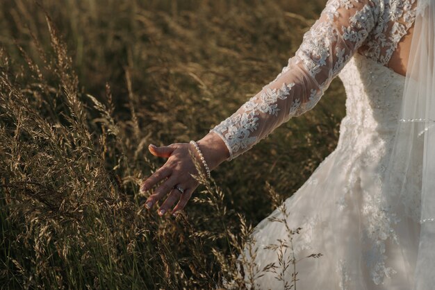 Novia caminando en un campo de trigo con un hermoso vestido de novia y una pulsera de perlas