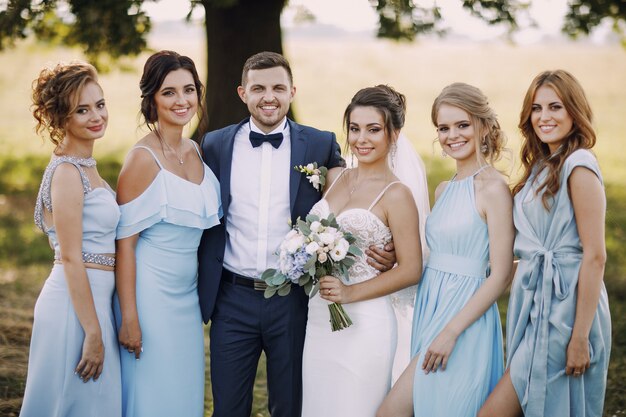 novia elegante y con estilo junto con sus cuatro amigas en vestidos azules y su marido