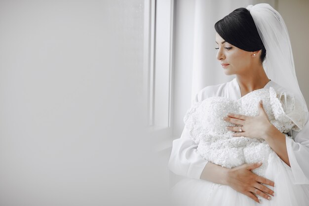 Una novia elegante y hermosa en casa de pie junto a la ventana