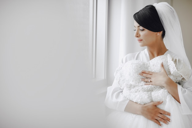 Una novia elegante y hermosa en casa de pie junto a la ventana